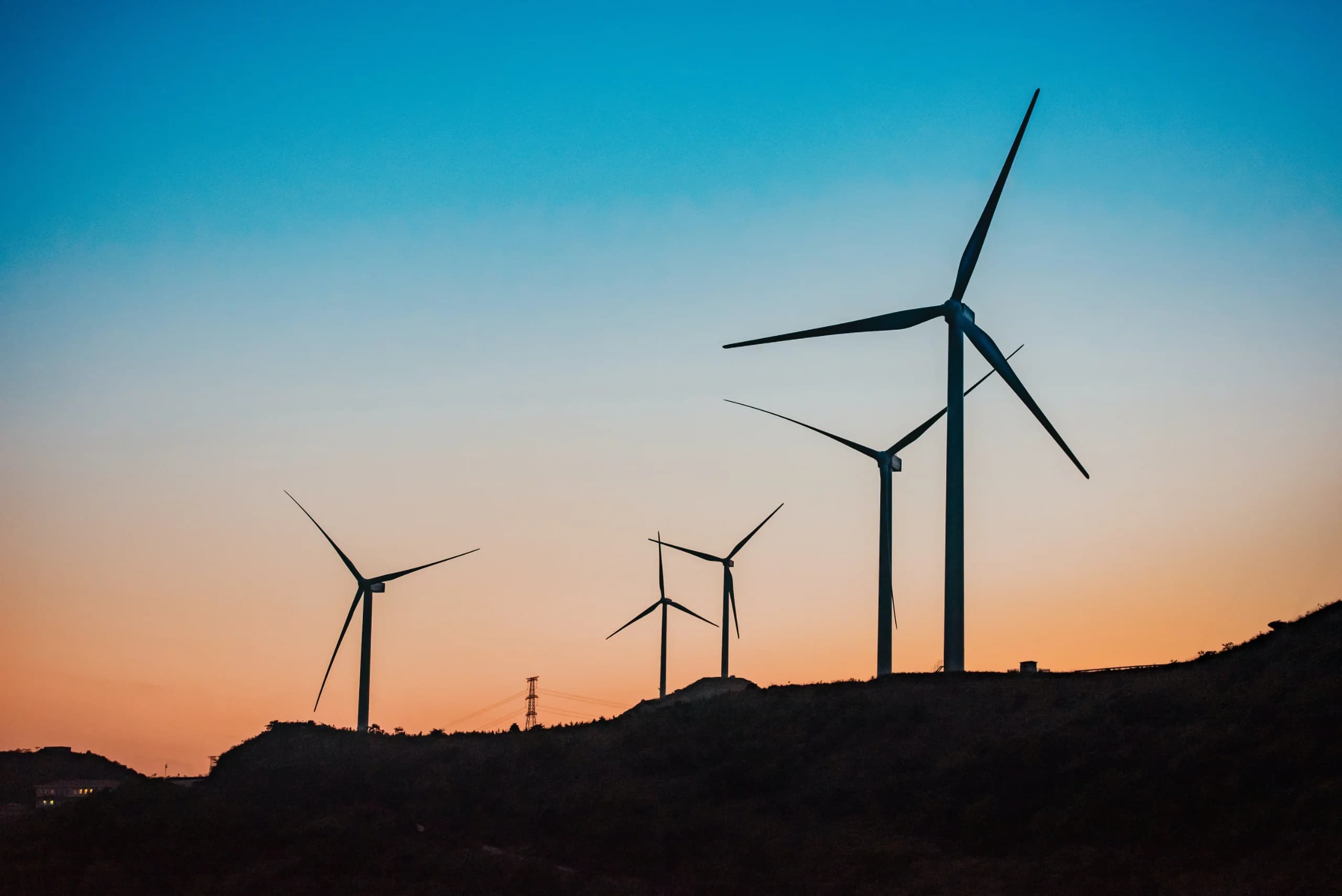 Four wind turbines silhouetted on a dark ridge against a blue-to-orange dusk sky