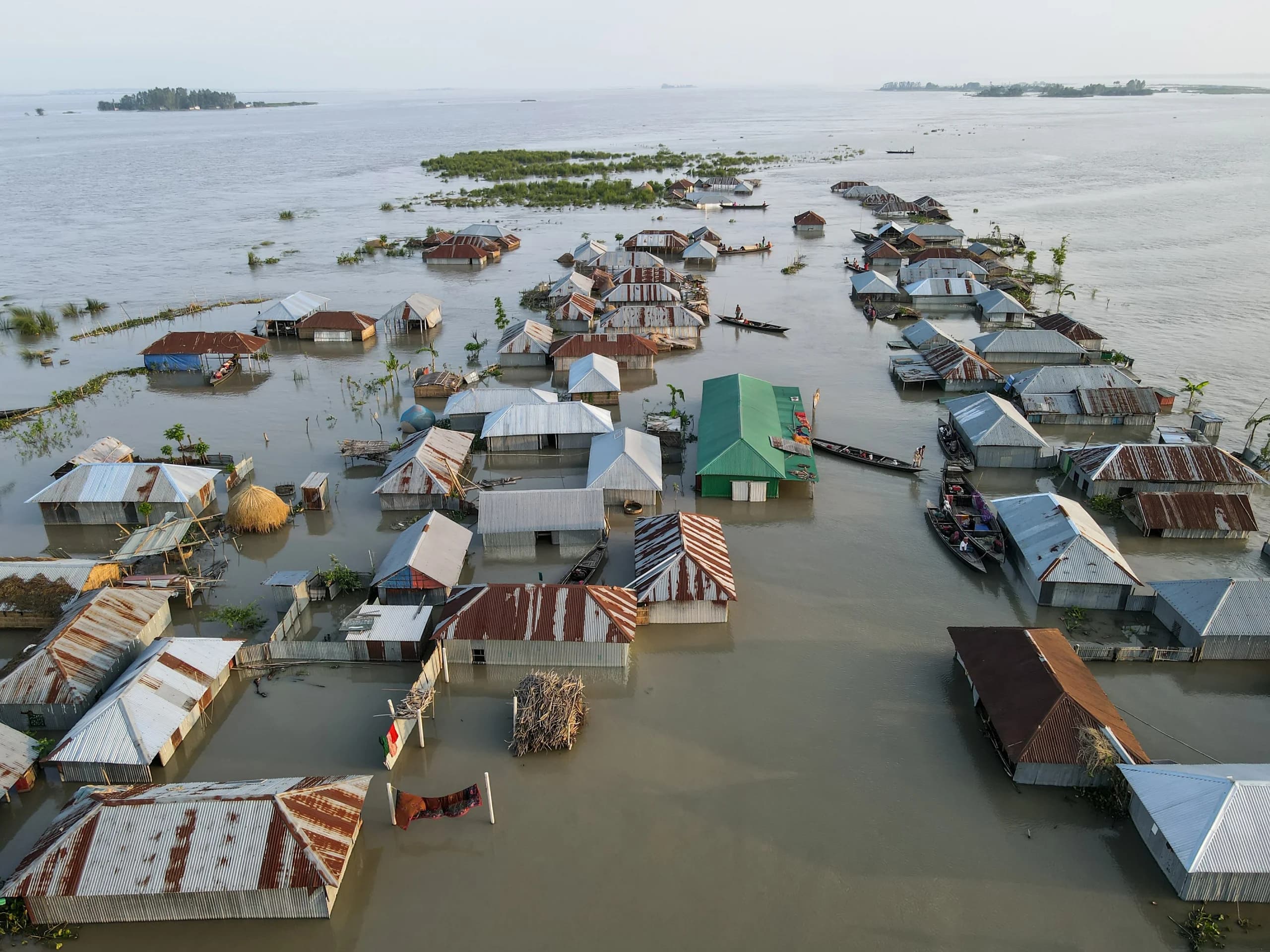 Aerial view of a flooded village, tin-roofed houses submerged to the eaves with small boats moving between them