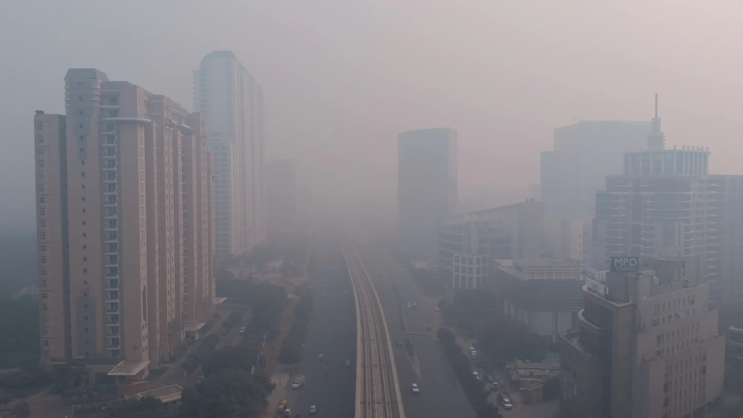 High-rise towers and an elevated metro line fading into thick grey smog over a city highway